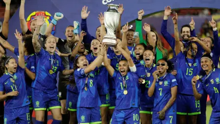 Marta y Angelina de Brasil levantan el trofeo mientras celebran con sus compañeras de equipo tras ganar la Copa América Femenina 2025.