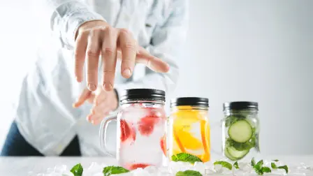 Hand takes one of rustic jars with cold fresh homemade lemonades from strawberry, orange, cucumber, ice and mint Close focus on first jar, action move, summer mood