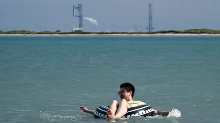 Un hombre nada en la playa de South Padre Island, Texas, con la nave espacial Starship de SpaceX.