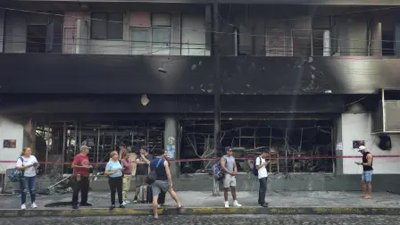 People stand next to a burned building in Puerto Vallarta, Jalisco state, Mexico, on February 23, 2026. Mexico has deployed 10,000 troops to quell clashes sparked by the killing of the country's most wanted drug lord, which have left dozens dead, officials said on February 23. Nemesio 