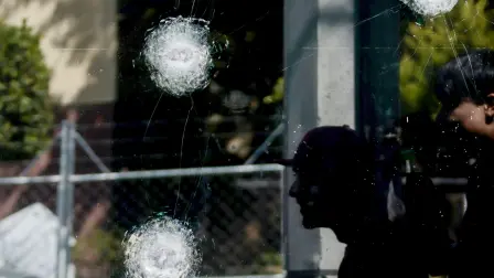 Young men walk past teh window of a police station with bullet impacts in Guadalajara, Jalisco, Mexico, on February 23, 2026, a day after clashes. Mexico has deployed 10,000 troops to quell clashes sparked by the killing of the country's most-wanted drug lord, Nemesio 
