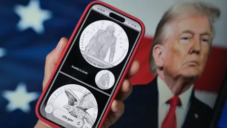 This illustration photo created on March 19, 2026 in Los Angeles shows a phone displaying the commemorative gold coin design marking America's 250th anniversary, approved by the United States Commission of Fine Arts, in front of a computer screen showing US President Donald Trump. An advisory commission hand-picked by President Donald Trump has approved the design of a commemorative gold coin featuring his image, officials said Thursday, in a move slammed by Democratic opponents. The US Commission of Fine Arts declined to comment when asked by AFP after several media outlets showed the proposed design in reporting on the approval. (Photo by Chris DELMAS / AFP) / -- IMAGE RESTRICTED TO EDITORIAL USE - STRICTLY NO COMMERCIAL USE --