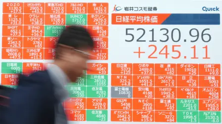 A man walks past an electronic quotation board displays numbers of the Nikkei Stock Average on the Tokyo Stock Exchange along a street in Tokyo on March 31, 2026. (Photo by Kazuhiro NOGI / AFP)