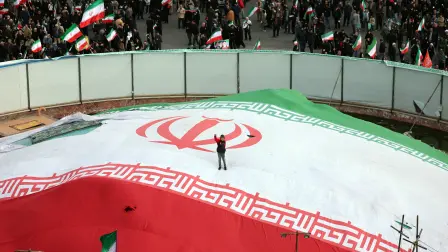 A boy raises his fist while standing on a giant Iranian flag during the funeral of Alireza Tangsiri, commander of the Iranian Revolutionary Guards' navy alongside others killed in US-Israeli strikes on Iran at Enghelab Square in Tehran on April 1, 2026. Iran confirmed on March 30 that an Israeli strike had killed the commander of the naval force of the Revolutionary Guards, who Israel had said was responsible for the blocking of the Strait of Hormuz. A statement carried by the Guards' Sepah News website said Alireza Tangsiri "succumbed to severe injuries" from the attack last week. (Photo by AFP) /