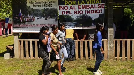 Unas jóvenes pasan junto a un cartel que dice: "¡De por vida, no a la represa del Río Indio!".