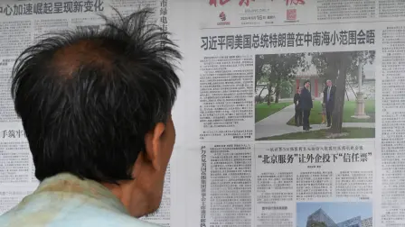 A man reads a newspaper with an article about the visit of US President Donald Trump to Zhongnanhai Garden, hosted by Chinas President Xi Jinping, at a newspaper display board in Beijing on May 16, 2026. (Photo by GREG BAKER / AFP)