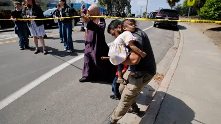 Un padre de familia carga a su hija para abandonar el Centro Islámico en donde ocurrió un tiroteo.