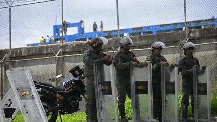 Members of the Bolivarian National Guard (GNB) stand guard as inmates clean the roof of the Internado Judicial Barinas (INJUBA) prison in the background, in Barinas, Venezuela, on May 25, 2026. More than 100 female detainees were transferred from a prison in Venezuela after hundreds of inmates took control of the facility, denouncing "torture" by prison authorities, who pledged to set up a "technical committee" to mediate, an independent observatory said on May 25. (Photo by Federico PARRA / AFP)