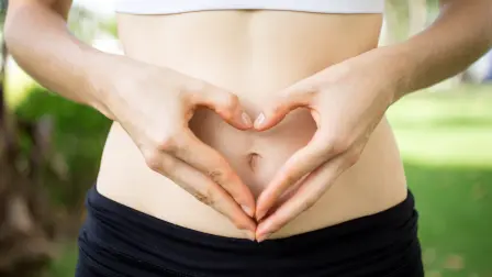 Close-up of female hands shaping heart on belly outdoors. Fitness and dieting concept