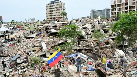 Members of a Mexican Army rescue unit and volunteers work amid the rubble of collapsed buildings as a Venezuelan flag stands in Caraballeda, La Guaira state, Venezuela, on July 3, 2026. The death toll from Venezuela's twin earthquakes has risen to 2,595, Interim President Delcy Rodriguez said on July 2. (Photo by MARTIN BERNETTI / AFP)