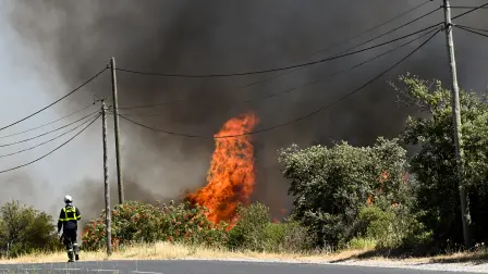 A French Civil Security firefighter walks on a road next to a wildfire near Ille-sur-Têt, southern France, on July 5, 2026. A wildfire broke out on July 4 at around 19h30 (1730 GMT) in a hard-to-reach massif near Trevillach, in the Pyrenees-Orientales department of southern France and spread rapidly overnight, burning through nearly 1,000 hectares by the morning of July 5, but the fire is no longer spreading freely, according to the prefecture. More than 580 firefighters have been deployed on the ground to fight the blaze. (Photo by Matthieu RONDEL / AFP)