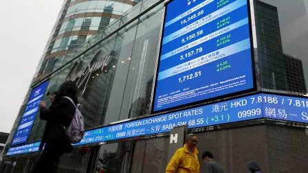 Personas pasan frente a pantallas que muestran el índice bursátil Hang Seng y los precios de las acciones en el exterior de Exchange Square en Hong Kong.
