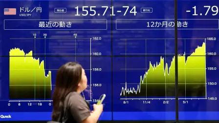 Una mujer frente a una pantalla electrónica que muestra gráficos sobre el tipo de cambio actual y reciente del yen japonés frente al dólar estadounidense.
