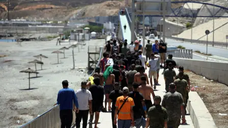 A group of migrants approach the border post to make their way back to Morocco, escorted by Spanish infantry soldiers, in the Spain's north African enclave of Ceuta, on August 2, 2026. At least 72 people died during the mass influx in recent days of migrants into Spain's Ceuta enclave, when tens of thousands of people mostly swam around the border post from Morocco, local officials said today. Most of the estimated 60,000 people who rushed into Spain's north African territory have returned to Morocco since the territory's largest mass migrant crossing. (Photo by Henry NICHOLLS / AFP)