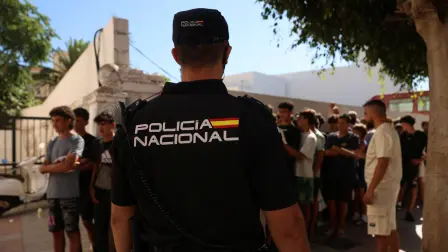 Un agente de policía monta guardia mientras niños migrantes hacen cola frente a una comisaría para ser registrados tras las travesías masivas de migrantes a pie y por mar desde Marruecos hacia territorio español.