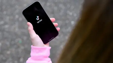 FILE PHOTO: A teenager poses for a picture with a phone displaying the TikTok logo, in Bonn, Germany, February 20, 2026. REUTERS/Jana Rodenbusch/File Photo