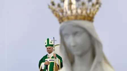 Papa León XIV de pie detrás de la estatua de la Virgen María coronada.