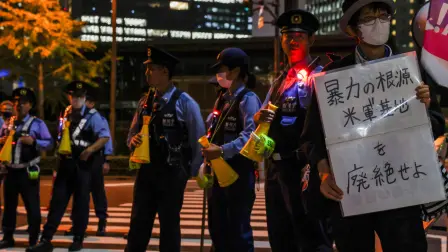 Un manifestante sostiene una pancarta que dice "Abolir las bases militares de EU, la raíz de la violencia", mientras agentes de policía montan guardia durante una protesta frente a la oficina del Primer Ministro tras la muerte de una mujer japonesa en Okinawa.