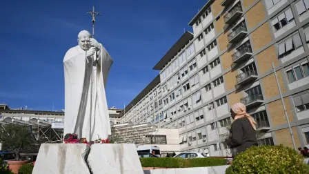 A woman prays at the statue of John Paul II outside the Gemelli University Hospital, where Pope Leo XIV is recovering after undergoing surgery to remove a cancerous tumour from his right lung, in Rome on October 14, 2026.  (Photo by Tiziana FABI / AFP)