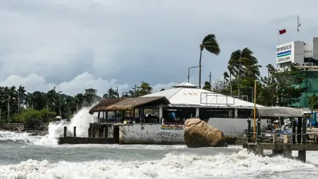 High waves crash against the waterfront as a red warning flag (R) flies outside the port captain's office in the tourist port of Acapulco, Guerrero state, Mexico, on September 28, 2026, warning vessels not to sail ahead of the arrival of Tropical Storm Rachel. (Photo by Francisco  ROBLES / AFP)