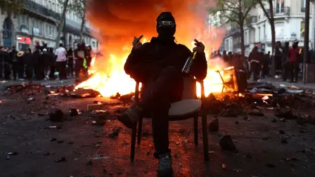 Un manifestante enmascarado se sienta en una silla frente a una barricada en llamas que bloquea una calle en medio de enfrentamientos durante una jornada de manifestaciones contra el costo de la vida.