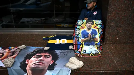 Un seguidor de la leyenda del fútbol argentino Diego Maradona se sienta junto a retratos y objetos conmemorativos en honor a Maradona frente al juzgado de San Isidro.