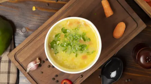 Chicken broth vegetable soup in disposable cup bowl served with green vegetables. image
