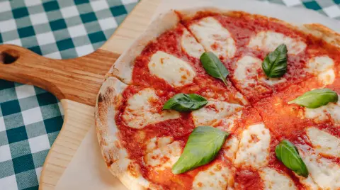 Neapolitan pizza on a cream sauce with ham, cheese, arugula, basil, tomatoes sprinkled with cheese on a wooden board on a tablecloth in a cell with a place for text