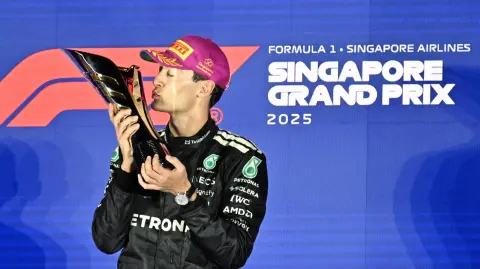 First-placed Mercedes' British driver George Russell celebrates on the podium after the Formula One Singapore Grand Prix night race at the Marina Bay Street Circuit in Singapore on October 5, 2025. (Photo by ROSLAN RAHMAN / AFP)