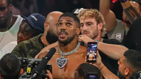 El YouTuber Logan Paul coloca una medalla alrededor del cuello del boxeador británico Anthony Joshua mientras celebra tras derrotar al boxeador e influencer estadounidense Jake Paul.