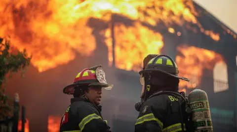 Bomberos frente a un edificio en llamas tras un incendio forestal en la región del Biobío.
