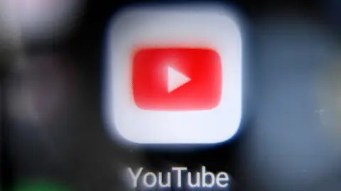 (COMBO) This combination of file photos created on January 21, 2026 shows the logo of Youtube social media on a smartphone screen in Moscow; and the BBC logo at the entrance of the BBC headquarters at Broadcasting House in central London. The BBC announced on January 21, 2026 a landmark new deal with US video platform YouTube which it said will showcase "the best homegrown storytelling and news from across" the British broadcaster's output. (Photo by Kirill KUDRYAVTSEV and Justin TALLIS / AFP)