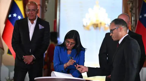 Venezuela's interim president Delcy Rodriguez (C) signs the amnesty law approved by the National Assembly, accompanied by the president of the Assembly Jorge Rodriguez (L) and the Minister of Interior, Justice and Peace Diosdado Cabello (back), at the Miraflores Palace in Caracas on February 19, 2026. Venezuela's Parliament unanimously approved on February 19 a historic amnesty law that is expected to lead to the release of hundreds of political prisoners after 27 years of Chavismo. (Photo by Juan BARRETO / AFP)