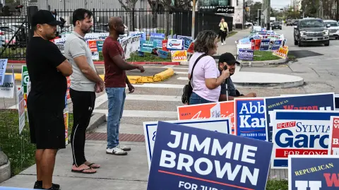 People walk by campaign signs near a polling location at West Gray Metropolitan Multi-Service Center on Election Day in Houston, Texas on March 3, 2026. Americans cast the first ballots of the primary season on Tuesday, kicking off a midterm cycle that could redraw the political map in Washington -- and shape how Donald Trump spends the remainder of his presidency. Texas anchors the opening slate, with voters in the second-largest state selecting their candidates in high-profile Senate primaries, offering an early test of how both parties position themselves for Trump's final two years. (Photo by RONALDO SCHEMIDT / AFP)