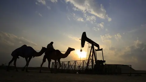 FILE- In this Sunday, Dec. 20, 2015 file photo, a man rides a camel through the desert oil field and winter camping area of Sakhir, Bahrain. OPEC nations have agreed in theory that they need to reduce their production to help boost global oil prices during a meeting in Algeria, but a major disagreement between regional rivals Saudi Arabia and Iran still may derail any cut. (AP Photo/Hasan Jamali, File) - FILE PHOTO
