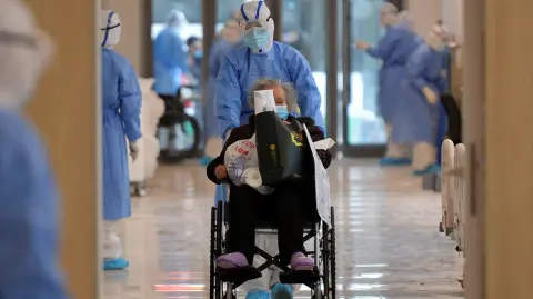 Medical worker in protective suit moves a novel coronavirus patient in a wheelchair at a hospital in Wuhan