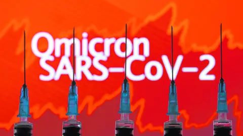 Syringes with needles are seen in front of a displayed stock graph and words 