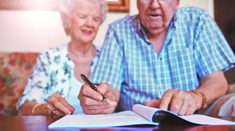 Senior couple signing will documents. Elderly caucasian man and woman sitting at home and signing some paperwork, focus on hands.
