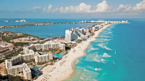 Aerial view of Cancun, Mexico showing luxury resorts and blue turquoise beach. showing people parasailing, swimming and tanning on the beach.