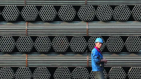 File photo of a worker walking past a pile of steel pipe products in China