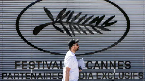 Un peatón pasa junto al logotipo del Festival de Cine de Cannes, en vísperas de la 78ª edición del Festival de Cine de Cannes, en Cannes, sur de Francia.