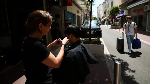 Una peluquera corta el pelo a una clienta en la calle debido a la falta de luz en su peluquería, tras un importante apagón, durante el 78º Festival de Cine de Cannes.