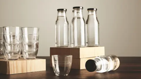 Perfect set of pure clean healthy water in transparent glass bottles and cups presented on wooden plates on tableOne cup and bottle in front close up