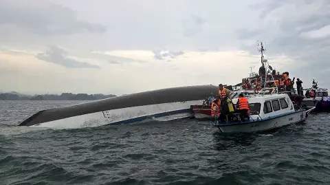 Personal de rescate reunido alrededor de un barco turístico volcado.