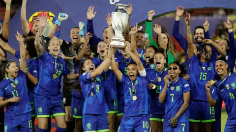 Marta y Angelina de Brasil levantan el trofeo mientras celebran con sus compañeras de equipo tras ganar la Copa América Femenina 2025.