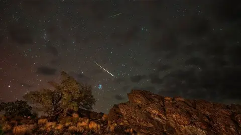 Lluvia de meteoros Perseidas atraviesan un cielo en 2024. A la izquierda, el resplandor rosáceo de la aurora. La galaxia de Andrómeda aparece en la parte superior, justo a la izquierda del centro.