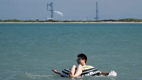 Un hombre nada en la playa de South Padre Island, Texas, con la nave espacial Starship de SpaceX.
