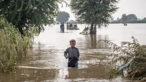 Un niño de siete años se abre paso a través de aguas de inundación hasta la altura de la cintura en Punjab, Pakistán.