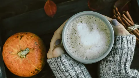 Spicy pumpkin latte on a wooden board with a sweater
