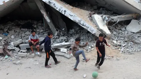 Niños palestinos juegan con una pelota entre montones de escombros y edificios dañados en Khan Younis, en el sur de la Franja de Gaza.
